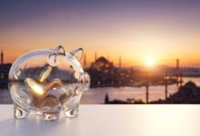 Un cerdito hucha de cristal moderno sobre una superficie blanca y limpia. Al fondo, la vista panorámica y desenfocada de la ciudad de Estambul, Turquía, al amanecer. La imagen simboliza el ahorro en tratamientos de implantes dentales al viajar.