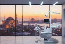 Una sala de tratamiento dental impecable y ultramoderna con equipos de última generación en primer plano. Un gran ventanal muestra una vista panorámica y desenfocada del horizonte de Estambul durante una hermosa puesta de sol.