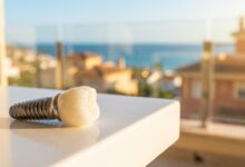 Un modèle d'implant dentaire de haute qualité au premier plan, avec en arrière-plan une vue floue et ensoleillée d'une ville côtière en Espagne, illustrant le concept de tourisme dentaire.