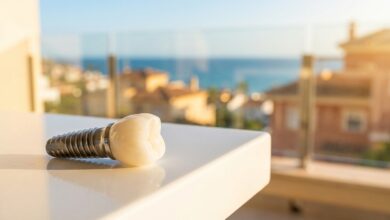 Un modèle d'implant dentaire de haute qualité au premier plan, avec en arrière-plan une vue floue et ensoleillée d'une ville côtière en Espagne, illustrant le concept de tourisme dentaire.