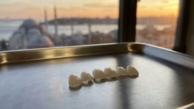 A close-up, photorealistic image of several pristine porcelain veneers on a clean surface, with the iconic skyline of Istanbul, Turkey, beautifully blurred in the background during a warm sunset.
