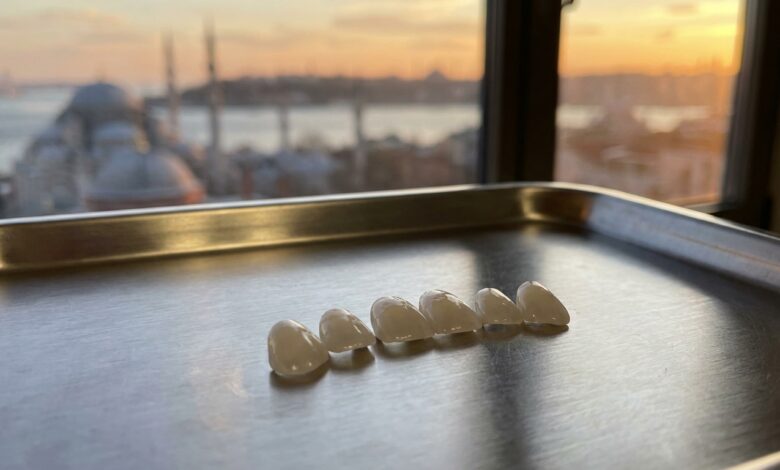 A close-up, photorealistic image of several pristine porcelain veneers on a clean surface, with the iconic skyline of Istanbul, Turkey, beautifully blurred in the background during a warm sunset.