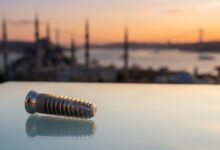 Un implante dental de titanio en primer plano, con el horizonte icónico y desenfocado de Estambul, Turquía, al atardecer como fondo.