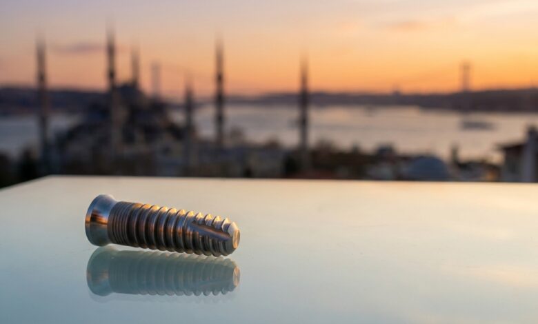 Un implante dental de titanio en primer plano, con el horizonte icónico y desenfocado de Estambul, Turquía, al atardecer como fondo.