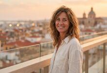 Une personne souriant avec satisfaction sur un balcon, avec en arrière-plan une vue floue et ensoleillée d'une ville côtière en Espagne, illustrant le concept de refaire ses dents à l'étranger.