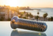 Un implant dentaire de haute technologie au premier plan, avec en arrière-plan une vue ensoleillée et floue d'une ville côtière espagnole, symbolisant le tourisme dentaire.