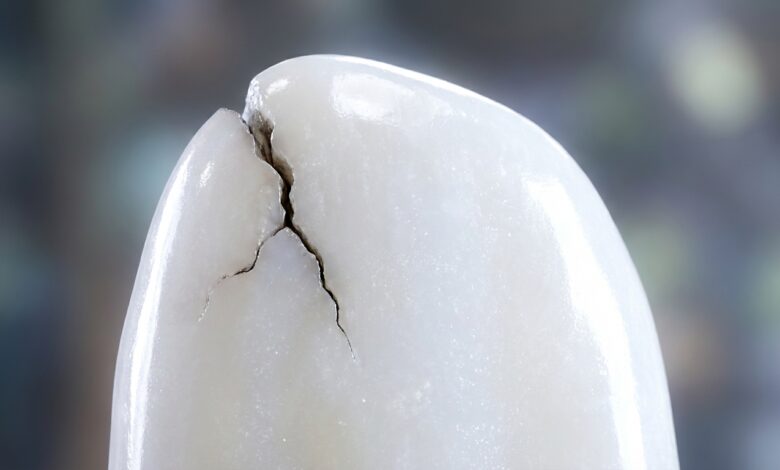 A photorealistic macro image of a perfect white enamel-like surface being compromised by a small, dark crack, symbolizing the beginning of a cavity.