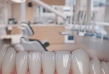 Primer plano de una boca con encías rosadas, sanas y perfectamente contorneadas alrededor de dientes blancos y brillantes, sobre un fondo borroso de una clínica dental moderna y luminosa que sugiere un entorno profesional y de alta calidad.