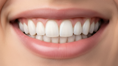 Primer plano fotorealista de una boca con una sonrisa blanca, perfecta y saludable, mostrando dientes alineados y encías rosadas. El fondo está suavemente desenfocado, revelando tonos cálidos de una escena arquitectónica española bañada por el sol.