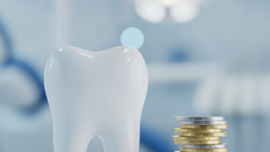 Primer plano de un diente molar blanco y saludable junto a una pila de monedas de oro y plata genéricas. El fondo está difuminado, mostrando el interior de una clínica dental moderna con iluminación suave.