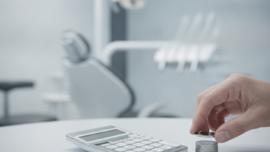 Una mano adulta coloca monedas sobre una superficie, con el fondo borroso de una clínica dental moderna y limpia, simbolizando la planificación financiera para tratamientos dentales en España.