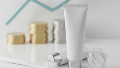 Una composición fotorealista de un cepillo de dientes blanco, pasta dental y hilo dental sobre una superficie limpia. En el fondo, elementos financieros borrosos como una pila de monedas simbolizan la prevención dental y el ahorro de costes.