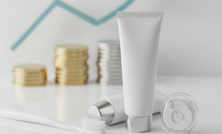 Una composición fotorealista de un cepillo de dientes blanco, pasta dental y hilo dental sobre una superficie limpia. En el fondo, elementos financieros borrosos como una pila de monedas simbolizan la prevención dental y el ahorro de costes.