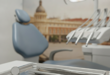 Primer plano de instrumentos dentales estériles y brillantes en una bandeja de acero inoxidable o una silla de dentista moderna y limpia con una luz quirúrgica, con un fondo muy borroso y desenfocado que sugiere un paisaje urbano o arquitectura clásica de Madrid al atardecer o durante el día.