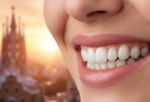 Imagen fotorealista de una boca con una sonrisa radiante y saludable, mostrando dientes blancos y naturales. Los labios están en un suave enfoque, transmitiendo confianza y bienestar. El fondo es un desenfoque artístico que sugiere el horizonte urbano de Barcelona, posiblemente con la luz cálida de un amanecer o atardecer. La iluminación es cinematográfica y limpia, destacando la calidad y la promesa de una restauración dental.