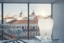 Una imagen fotorealista de un diente blanco y radiante que simboliza la salud dental, situado en un entorno de clínica moderna y limpia. Al fondo, a través de una ventana borrosa, se distingue un perfil urbano genérico de Madrid con arquitectura característica, sin texto visible. La escena enfatiza la odontología de calidad en la capital española.