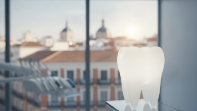 Una imagen fotorealista de un diente blanco y radiante que simboliza la salud dental, situado en un entorno de clínica moderna y limpia. Al fondo, a través de una ventana borrosa, se distingue un perfil urbano genérico de Madrid con arquitectura característica, sin texto visible. La escena enfatiza la odontología de calidad en la capital española.