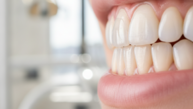 Imagen detallada y fotorrealista de dos dientes. Un diente muestra una fina carilla dental translúcida en la superficie frontal, y otro diente adyacente exhibe una corona dental completa que cubre toda su estructura, ambos con un acabado natural y saludable. Fondo borroso de clínica dental moderna.