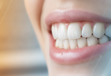Primer plano de dientes y encías sanos, blancos y brillantes, con un aspecto impecable en un entorno dental moderno. El fondo está suavemente desenfocado con gradientes de color abstractos y sutiles, que sugieren una comparación o dualidad de opciones.